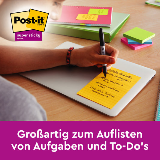 Eine Person schreibt auf einem großen, linierten Post-it® Super Sticky Note (127 mm x 203 mm) der 3M Deutschland GmbH, das auf einem geschlossenen Laptop liegt. Text: "Großartig zum Auflisten von Aufgaben und To-Do's.
