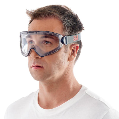 Un homme porte les lunettes de protection 3M™ modèle 2891 avec Scotchgard™ Protector antibuée, ventilation indirecte et verre transparent, fabriquées par 3M Deutschland GmbH. Les lunettes ont une bande réglable noire et grise et sont présentées sur un fond blanc.