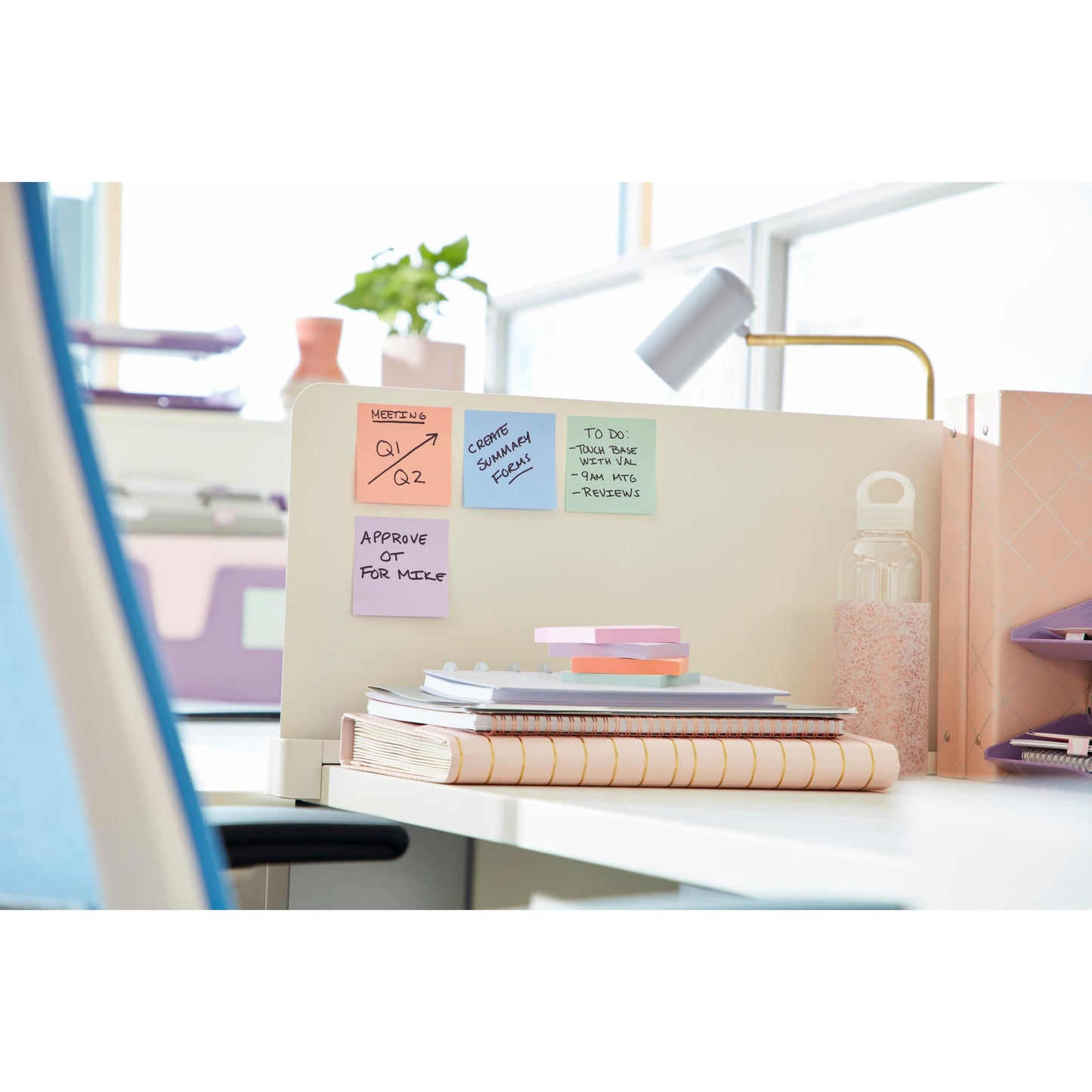 Un espace de travail de bureau bien rangé avec des Post-it® Super Sticky Notes (76 mm x 76 mm, 90 feuilles/bloc, 100% PEFC) de 3M Deutschland GmbH sur une cloison, avec des cahiers, des papiers empilés, une bouteille d'eau en verre et des classeurs organisés en arrière-plan.