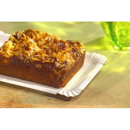 Un gâteau aux amandes carré repose sur une assiette PAPSTAR GmbH rectangulaire 24x33 cm, en carton "pure", blanche (125 pièces), avec un objet en verre vert qui se floute en arrière-plan.