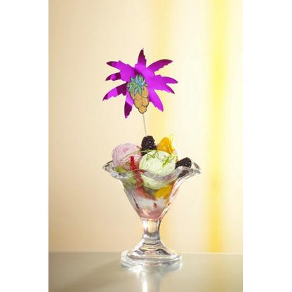 Eine gläserne Dessertschale mit leuchtendem Eis, Früchten und Brombeeren wird mit einem Deko-Picker "Palmblätter" 19,5 cm (farbig sortiert) der PAPSTAR GmbH aus dem 50-teiligen Papptray-Set vor einem zartgelben Hintergrund elegant verziert.