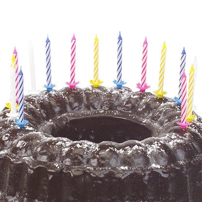 Ein Schokoladenkuchen mit Puderzucker bestreut und dekoriert mit zehn PAPSTAR Geburtstagskerzen 6 cm, farbig sortiert mit Halter (von PAPSTAR GmbH) in verschiedenen Farben.