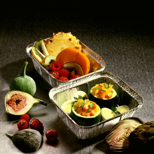 Deux plateaux Starpak 25 en aluminium avec couvercles revêtus de PP sont remplis de fruits frais comme kiwi, ananas, figues, baies et de légumes comme courgette et melon sur une surface grise - idéal pour le catering ou à emporter.