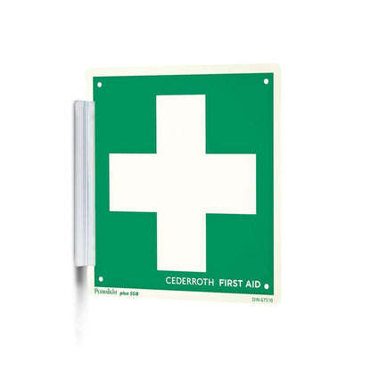Ein grün-weißer "Clip signieren | Packung (1 Stück)" von Orkla Wound Care AB mit einem großen weißen Kreuz und dem Schriftzug "Cederroth First Aid" wird wie ein Signaturstempel mit einer Metallhalterung an der Wand befestigt und ist so am Arbeitsplatz gut sichtbar.
