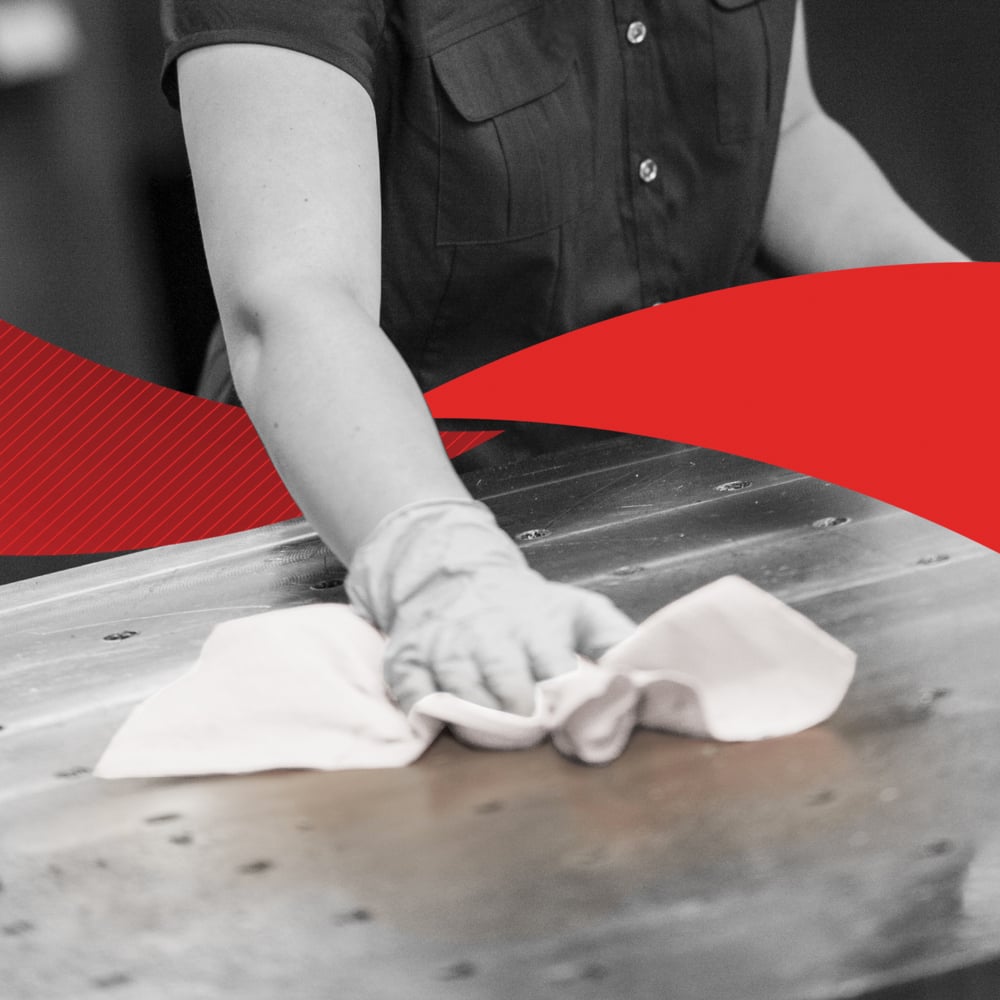 Eine Person in einem kurzärmeligen Hemd wischt eine große Metalloberfläche mit einem Tuch ab, möglicherweise ein Kimberly-Clark GmbH WypAll® X60 General Clean aus der BRAG™ Box (41,80 cm x 28,30 cm); das Bild ist hauptsächlich schwarz-weiß mit einer kräftigen roten Diagonale in der Mitte.