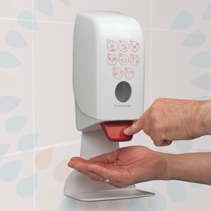 Une personne appuie sur un levier rouge d'un distributeur mural de désinfectant pour les mains Kleenex® Extra Gel (Kimberly-Clark GmbH) et distribue un désinfectant pour les mains clair sur sa main. Une instruction illustrée est visible sur le devant, avec des carreaux à motifs en arrière-plan.