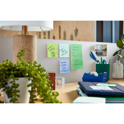 Sur un bureau est accroché un bloc de Post-it® Super Sticky Notes (101x101 mm, 70 feuilles, PEFC) de 3M Deutschland GmbH comme aide-mémoire sur le mur. Une lampe, une plante verte, une tasse avec des stylos, des fournitures de bureau et une photo sont également visibles.