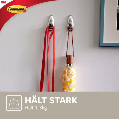 Deux crochets en métal Command™ "classique" de 3M Deutschland GmbH sont montés sur un mur blanc et tiennent une laisse rouge et un parapluie à motifs jaunes. Le texte indique : "TIENS FORT Supporte 1,3 kg" et montre le logo Command.