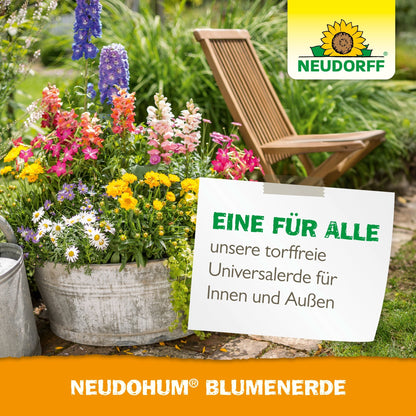 Un seau en métal avec des plantes de jardin colorées est posé sur un chemin de jardin à côté d'une chaise pliante en bois. Un panneau fait la promotion de la NeudoHum BlumenErde sans tourbe du Neudorff Shop pour l'intérieur et l'extérieur.