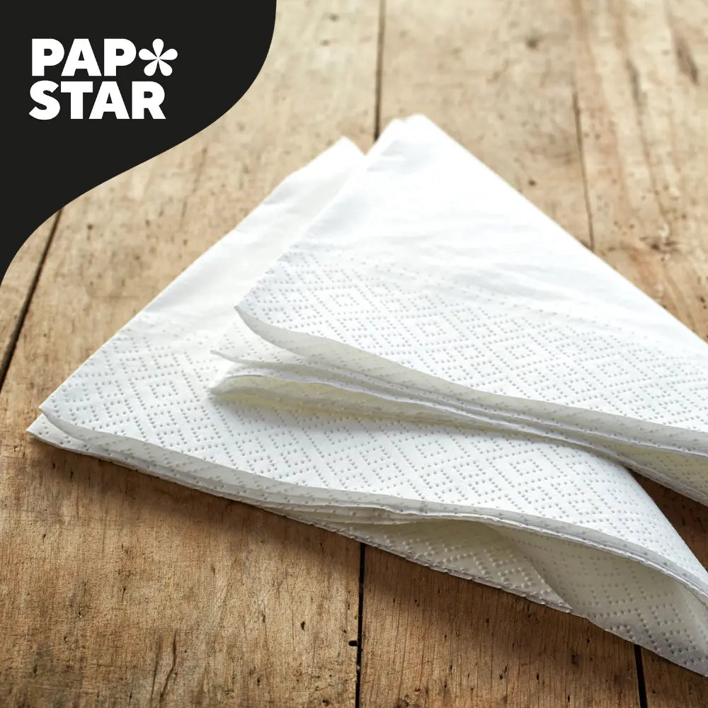 Drei gestapelte weiße Papierservietten mit einem dezenten Rautenmuster sind auf einer rustikalen Holzoberfläche abgebildet. In der oberen linken Ecke befindet sich das Markenlogo 