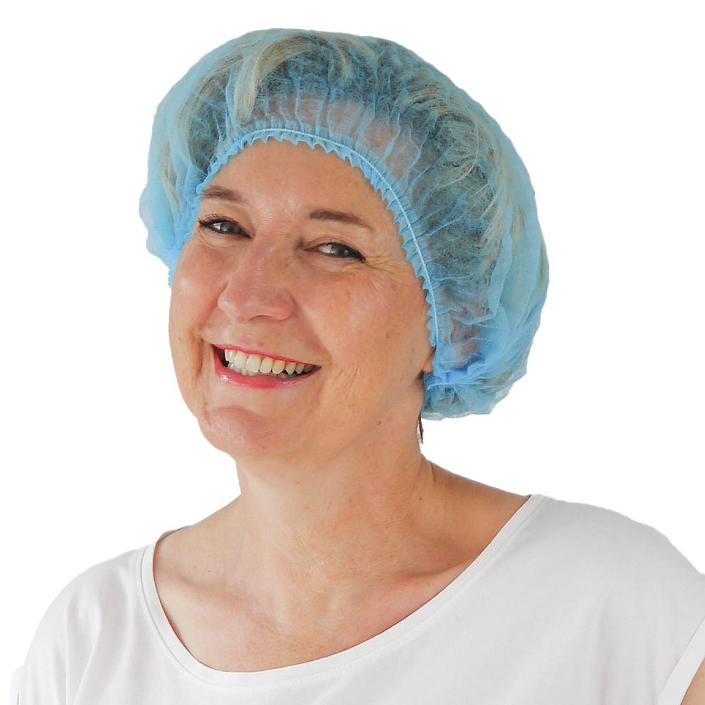 Eine Frau lächelt vor weißem Hintergrund und trägt eine ARNOMED COVER PP-KLIPPHAUBE XL Einmalklipphaube aus PP-Vlies (55cm Umfang) der ARNOWA GmbH und ein weißes Hemd - ideal für die Einhaltung von Hygienestandards.