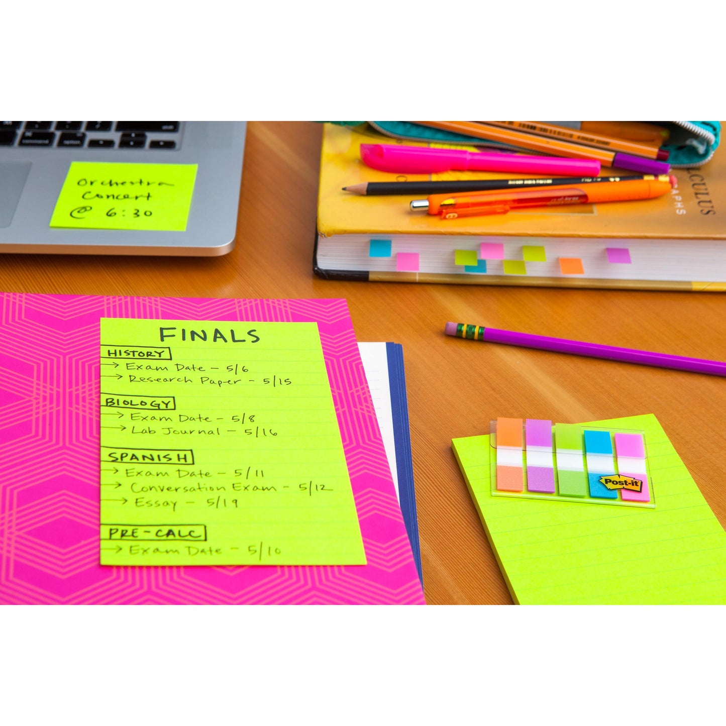 Sur une table d'étude se trouvent des livres, des stylos, une chemise rose avec le planning des examens finaux sur papier néon et des Post-it® Super Sticky Notes en grand format (101 mm x 101 mm, 70 feuilles/bloc, 100% PEFC) de 3M Deutschland GmbH, tout est soigneusement disposé sur du bois.