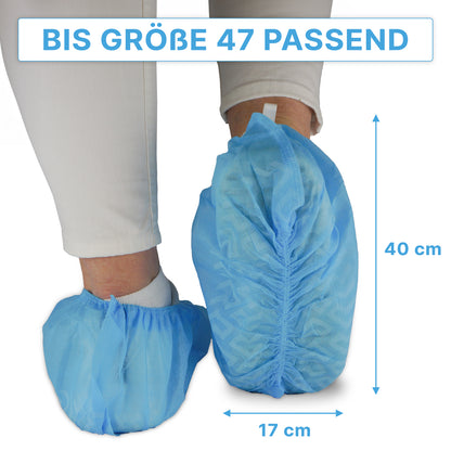 Une personne porte des surchaussures bleues ARNOMED ABS de ARNOWA GmbH par-dessus un pantalon blanc ; ces surchaussures jetables antidérapantes conviennent jusqu'à la taille 47 et mesurent environ 40×17 cm, comme indiqué par les flèches. Paquet : 100 pièces.