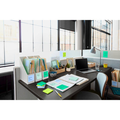 Un espace de bureau moderne avec un bureau bien rangé, un ordinateur portable, des carnets, des classeurs, un verre d'eau, une plante et une lampe. Sur le bureau se trouvent des Post-it® Super Sticky Notes de 3M Deutschland GmbH en grand format (101 mm x 101 mm). De grandes fenêtres laissent entrer la lumière naturelle.