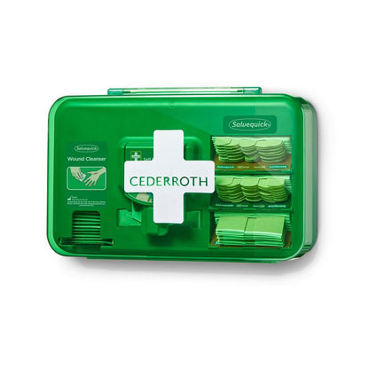 Illustré est un distributeur de soins des plaies Cederroth vert de Orkla Wound Care AB (20,3x30,6x15,5 cm) avec une croix blanche, contenant des fournitures visibles à travers le devant en plastique transparent comme des bandages et des nettoyants, et livré en set de sachets en plastique.
