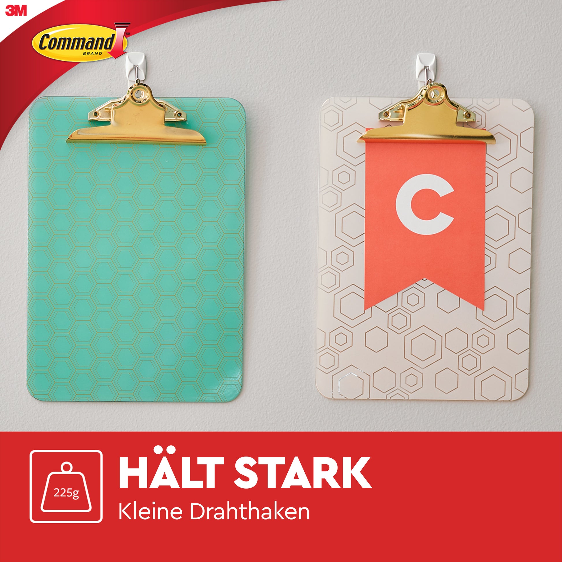Zwei Klemmbretter hängen an einer grauen Wand mit weißen Command™ Small Drahthaken (17067) von 3M Deutschland GmbH. Ein Klemmbrett ist türkis mit Sechsecken, das andere weiß mit einem orangefarbenen "C". Text: "HÄLT STARK Kleine Drahthaken 225g.