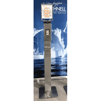 Der Dr. Schnell Edelstahlspender V10 touchless von DR.SCHNELL GmbH & Co. KGaA steht mit einem orangefarbenen Grafikdisplay vor einer blauen Kulisse mit Eisbergen und Wasserbildern.