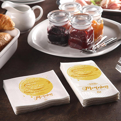 Une table de petit-déjeuner avec des croissants, une carafe et 200 serviettes PAPSTAR (3 plis 1/4 de pli, 24x24 cm) de la société PAPSTAR avec l'inscription « Bonjour », accompagnée de pots de confiture et de trois fourchettes pour un repas matinal convivial.