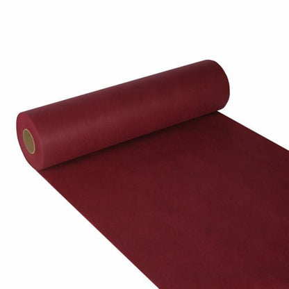 Un chemin de table Starpak partiellement déroulé, non-tissé semblable à du tissu « soft selection » (24m x 40cm), en rouge foncé, est représenté sur un fond blanc avec une surface lisse et mate - idéal pour une décoration stylée. Le papier est enroulé autour d'un noyau en carton.