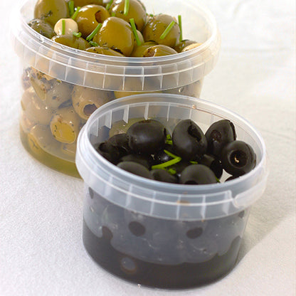 Deux pots à charcuterie transparents Starpak 50, pots ronds en PP avec fermeture d'authenticité - l'un rempli d'olives vertes et d'herbes, l'autre avec des olives noires et des brindilles d'herbes - sont posés sur un fond clair.