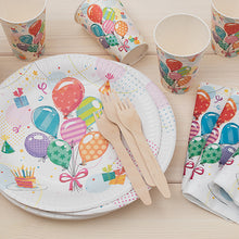 PAPSTAR 50 assiettes, carton rond Ø 23 cm de la PAPSTAR GmbH, avec des gobelets et des serviettes aux motifs de ballons et de cadeaux ainsi que des fourchettes et couteaux en bois, arrangés sur du bois clair pour une fête écologique.