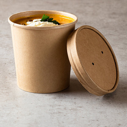 Le gobelet à soupe Starpak 25, carton rond Ø 11,5 cm brun de Starpak est rempli de soupe à l'orange, crème et persil - parfait pour savourer vos soupes à emporter sur une surface gris clair, le couvercle repose à côté du gobelet.