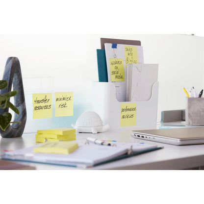 Ein moderner Bürotisch mit einem Laptop, Schreibwaren, einer weißen Dokumentenablage, einer kleinen weißen Schildkrötenfigur und 3M Deutschland GmbH Post-it® Super Sticky Notes Würfel (Gelb, 76x76 mm) mit den Aufschriften "Ressourcen übertragen", "Risiko minimieren" und "Leistungsbeurteilung".