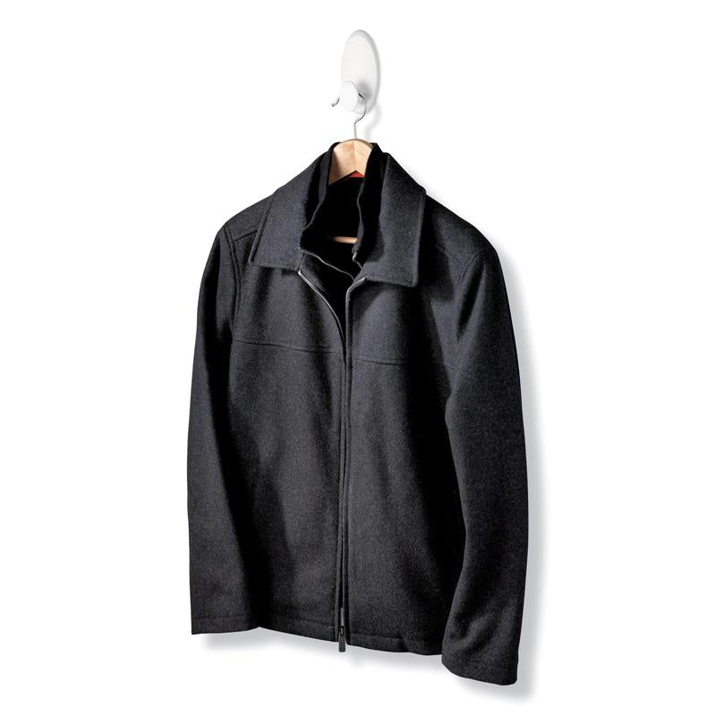 Une veste noire avec fermeture éclair et col est suspendue à un cintre en bois du crochet à vêtements Command™ 17019-FGN, permettant une fixation murale sans perçage, devant un fond blanc uni.