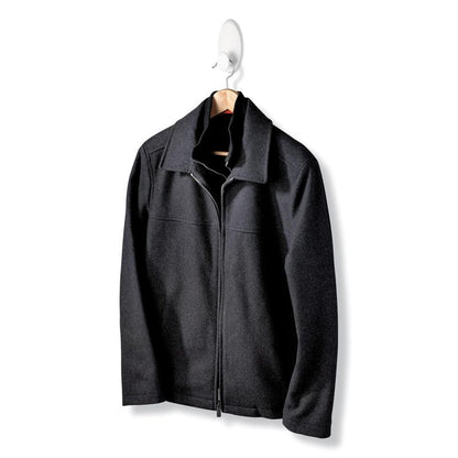 Une veste noire avec fermeture éclair et col est suspendue à un cintre en bois du crochet à vêtements Command™ 17019-FGN, permettant une fixation murale sans perçage, devant un fond blanc uni.
