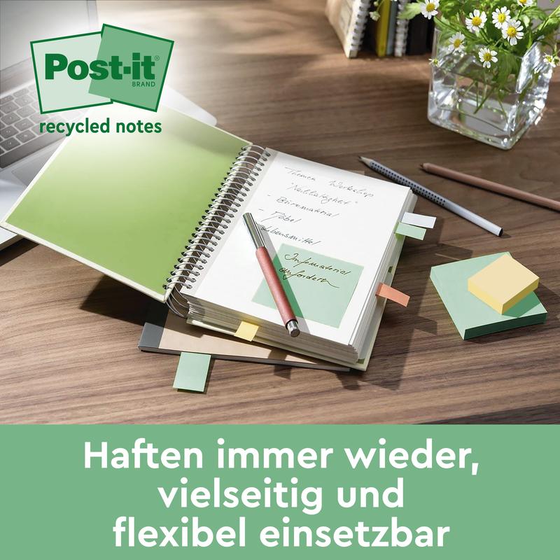Un bureau avec un carnet ouvert avec des notes de recyclage Post-it® vertes (76 mm x 127 mm, 100 feuilles/bloc, 100% PEFC) de 3M Deutschland GmbH, un stylo, des notes Post-it® de différentes couleurs, un clavier, un vase en verre avec des plantes et un texte allemand au fond.