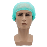 Sur un fond blanc sobre figure une tête de poupée de couleur beige, au visage impassible et aux cheveux courts et foncés, recouverte d'un bonnet à clip AMPri MED-COMFORT de 52 cm, de couleur vert clair, en polypropylène, fabriqué par la société AMPri Handelsgesellschaft mbH. Ce bonnet offre une protection hygiénique.