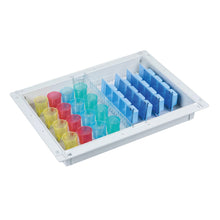 Das weiße Novocal Blistermodul (ABS, 300 x 400 x 50 mm) für 32 Bewohner fasst farbcodierte Zylinder - gelb, rot, blau - und verfügt über vertikale blaue Trennwände auf der rechten Seite für ein platzsparendes Medikamentenaufbewahrungssystem.