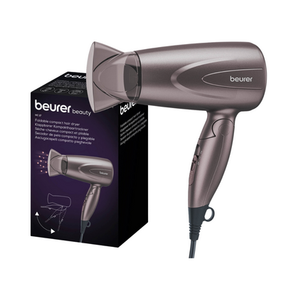 Image d'un sèche-cheveux compact pliable Beurer HC 17 à côté de son emballage. Le sèche-cheveux de Beurer GmbH est gris et possède une poignée pliable, ce qui souligne son design pratique en tant que sèche-cheveux compact. Sur l'emballage, on peut voir l'image du produit et la description du produit qui mettent en avant ses performances impressionnantes.