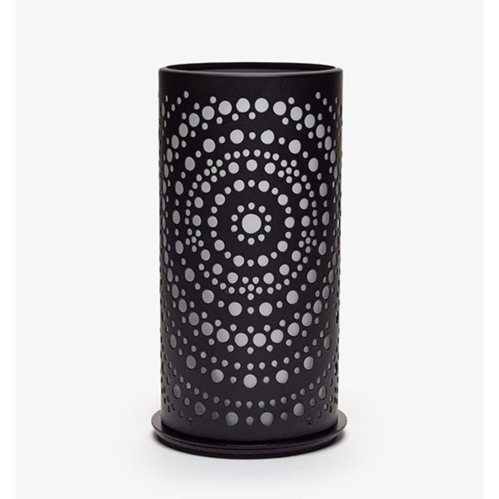 Un vase cylindrique noir avec des perforations circulaires en cercles concentriques, créant un design symétrique qui rappelle le design moderne, similaire au photophore Billy en métal de Duni GmbH, se trouve devant un fond blanc simple.