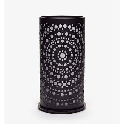 Un vase cylindrique noir avec des perforations circulaires en cercles concentriques, créant un design symétrique qui rappelle le design moderne, similaire au photophore Billy en métal de Duni GmbH, se trouve devant un fond blanc simple.