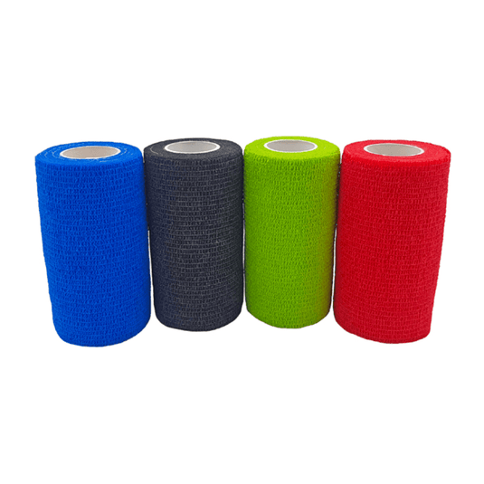 Quatre rouleaux de bandage auto-adhésif Holthaus VliVet® destiné au secteur vétérinaire, fabriqué par Holthaus Medical GmbH & Co. KG, sont alignés les uns à côté des autres. De gauche à droite, les couleurs sont le bleu, le noir, le vert et le rouge. Ces bandages présentent une surface texturée et une forme cylindrique avec un cœur blanc à l'intérieur, ce qui les rend idéaux pour les soins des sabots en milieu vétérinaire.