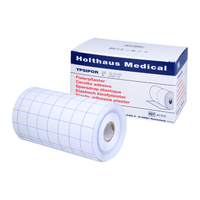 Eine Rolle Holthaus Medical Fixierpflaster mit Gittermuster liegt vor der Schachtel mit der Aufschrift „Holthaus Ypsidor“. Die mehrsprachige Beschreibung auf der Verpackung unterstreicht die vielseitigen Anwendungsmöglichkeiten.