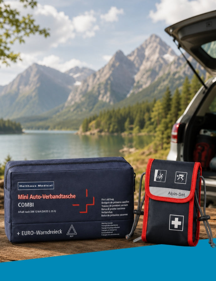 Banner von Holthaus Medical mit einer dunkelblauen Mini-Auto-Verbandtasche „COMBI“ und einem rot umrandeten „Alpin-Set“ auf einem Holztisch. Im Hintergrund stehen ein geöffnetes Auto sowie eine Berg- und Seenlandschaft. Links befindet sich eine dunkelblaue Fläche mit der weißen Aufschrift „Holthaus Medical“.