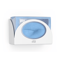 Ein Tork 655100 Small Pack Papierspender Performance W8 von Tork - Essity Professional Hygiene Germany GmbH, der hygienischen Schutz bietet, hält einen Stapel blauer Einwegtücher. Ein Tuch ist teilweise durch die Öffnung des Spenders gezogen. Das „Tork“-Logo ist sowohl auf dem schlanken Spender als auch auf der Verpackung der Tücher deutlich zu sehen.