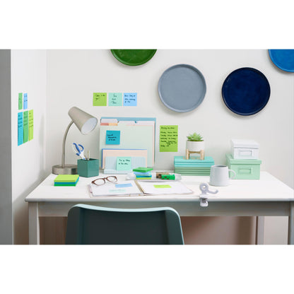 Un bureau blanc bien rangé avec des fournitures de bureau organisées, y compris des Post-it® Super Sticky Notes en grand format (101x101 mm, 70 feuilles/bloc, 100% PEFC) de 3M Deutschland GmbH, des classeurs, des articles de papeterie, une lampe, une plante et des cartons. Décor rond coloré et notes adhésives sur le mur.