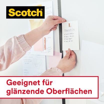 Eine Person klebt einen Zettel mit Scotch® Crystal Klebeband (12 mm x 10 m, mit Handabroller) von 3M Deutschland GmbH an eine weiße Wand. Weitere Zettel sind ebenfalls an die Wand geklebt. Im Bild steht: "Geeignet für glänzende Oberflächen.