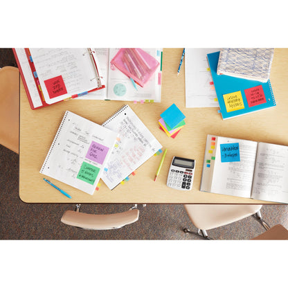 Vue de dessus d'une table de classe avec des cahiers ouverts, une calculatrice, des stylos, des manuels scolaires, des dossiers certifiés PEFC et des Post-it® Notes Energetic Collection 3M (76 mm x 127 mm, 100 feuilles/bloc, 6 blocs/paquet). Trois chaises entourent la table.