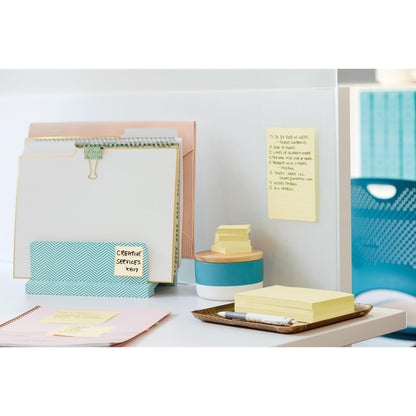 Un bureau bien rangé avec des classeurs, un bloc-notes, 3M Post-it® Super Sticky Notes Jaune (47,6x47,6 mm, 21+3 Pack promo), un stylo, une petite boîte, un plateau ; une liste de tâches est fixée à la cloison. Une chaise de bureau bleue se trouve à l'arrière-plan.