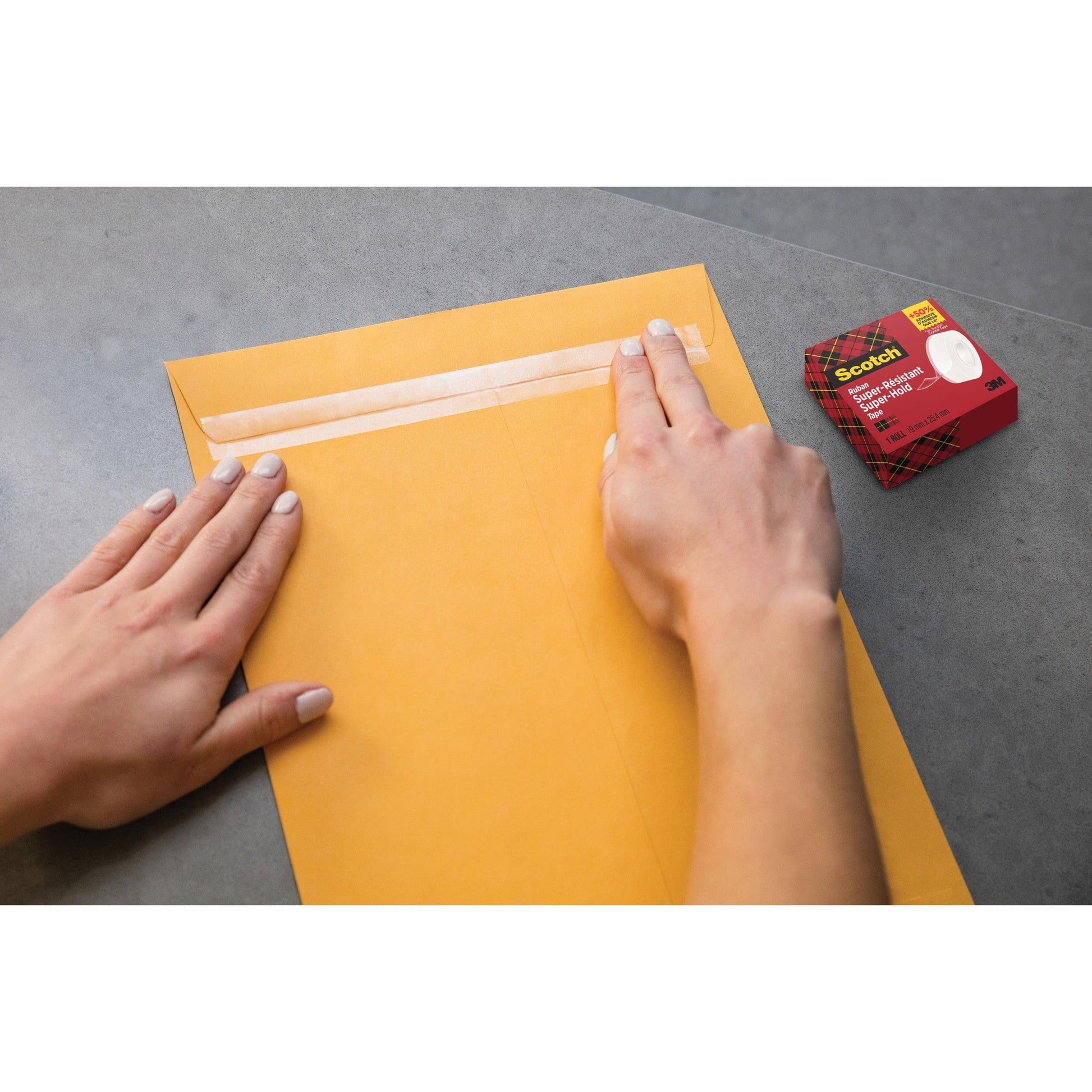 Jemand verschließt einen großen braunen Umschlag mit Scotch® Super-Hold Secure Tape (19 mm x 25,4 m, 1 Rolle) der 3M Deutschland GmbH; das Paket liegt auf einer grauen Fläche in der Nähe.