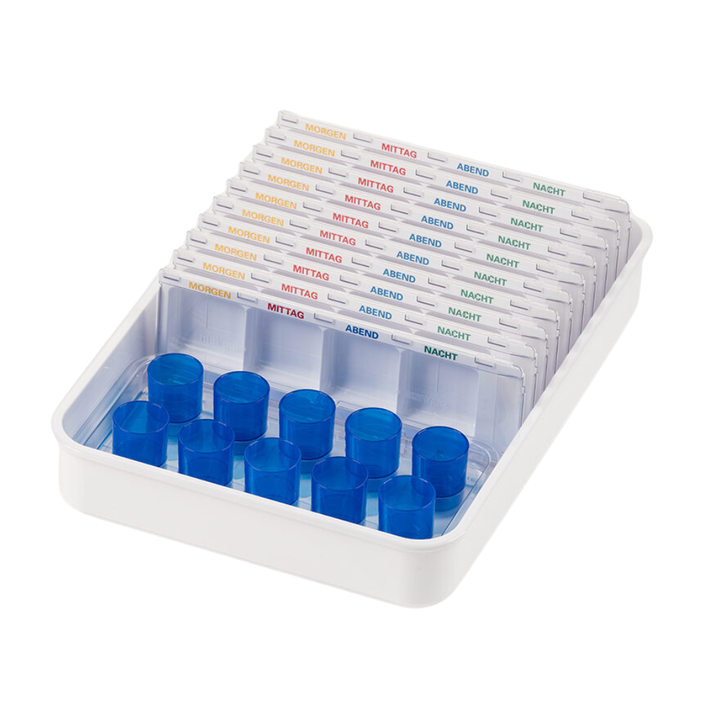 Un plateau de gobelets distributeurs Melipul blanc de Helmut Schwarz GmbH contient plusieurs distributeurs de pilules transparents, faisant partie d'un système d'organisation de médicaments, étiqueté avec des mots allemands pour les moments de la journée : « Matin », « Midi », « Soir », « Nuit ». Chaque distributeur réutilisable dispose de fentes pour les pilules et de couvercles bleus d'un côté.