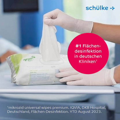 Eine Person zieht ein Desinfektionstuch aus einer Packung Schülke mikrozid® universal wipes Green Line auf dem Tisch. Ein rosa Kreis rühmt es als Nr. 1 für Flächendesinfektion in deutschen Kliniken und betont damit die Infektionsprävention. In der oberen rechten Ecke steht „Schülke & Mayr GmbH“, ein kleiner Text weist auf die leicht alkoholische Schnelldesinfektionsformel hin.